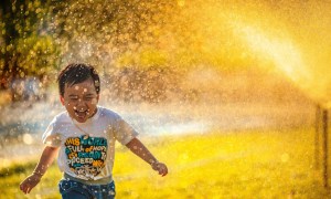 Toddler on lawn running past sprinkler