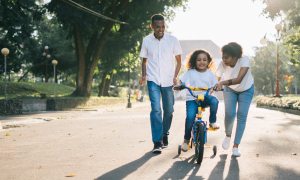 Parents teaching their daughter how to ride a bike with training wheels