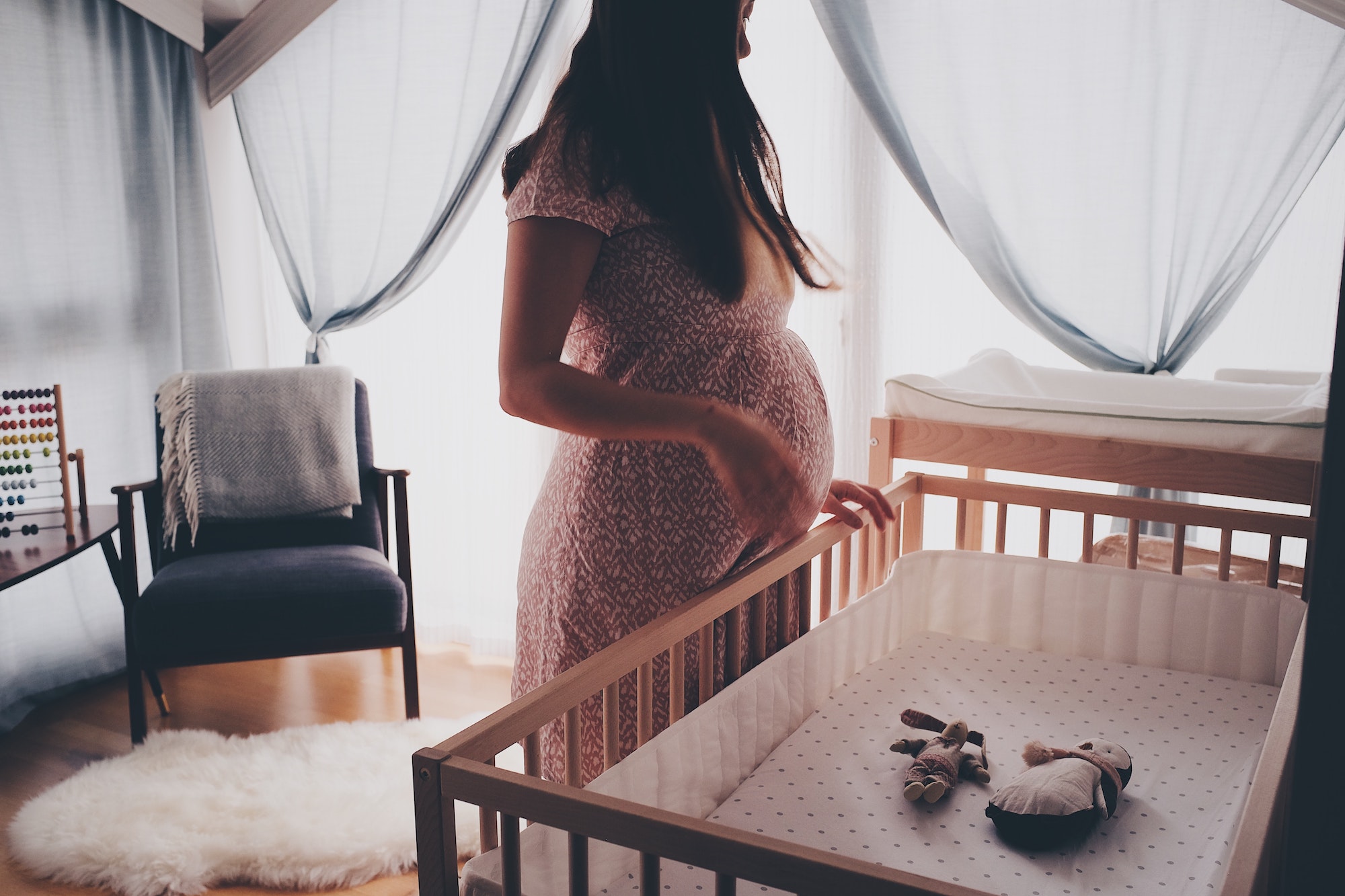 Pregnant woman standing over wooden crib in rustic nursery