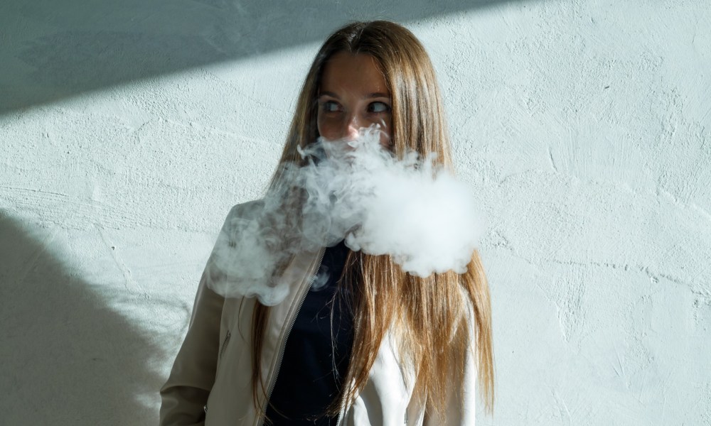 Teen girl vaping near a blue wall