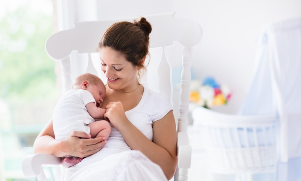 Mother holds her baby near a crib