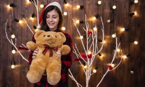 Teenager holding a teddy bear in front of a Christmas tree and lights