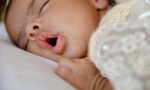 Baby sleeping in a bed with their mouth open