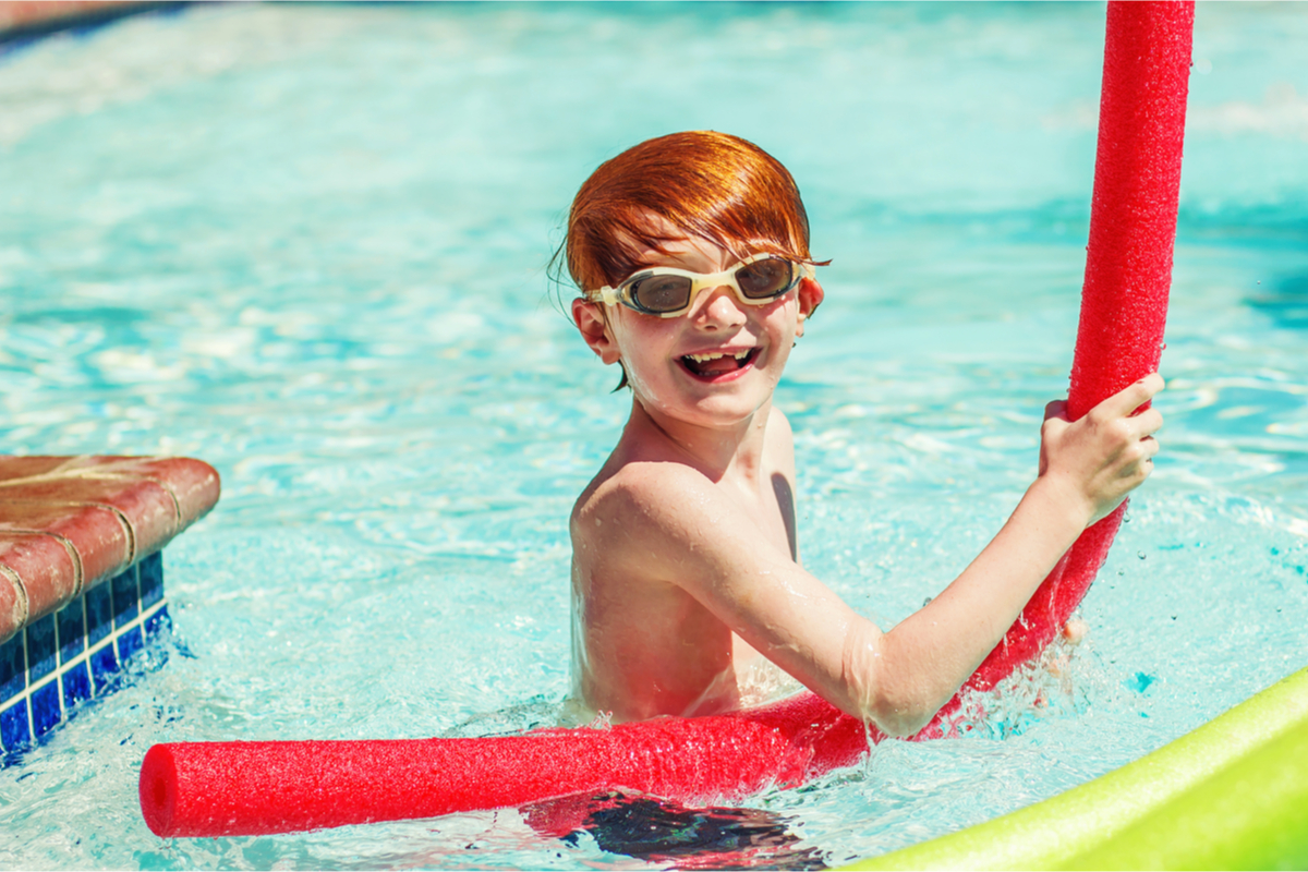 Smiling boy swimming with pool noodle
