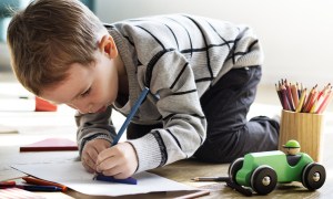 Little boy drawing in an art book with colored pencils