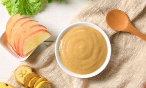 A table with baby food ingredients on it and a bowl of baby food puree.