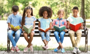 Five kids reading on a bench outside.