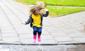 Little girl with rubber boots jumping in a puddle