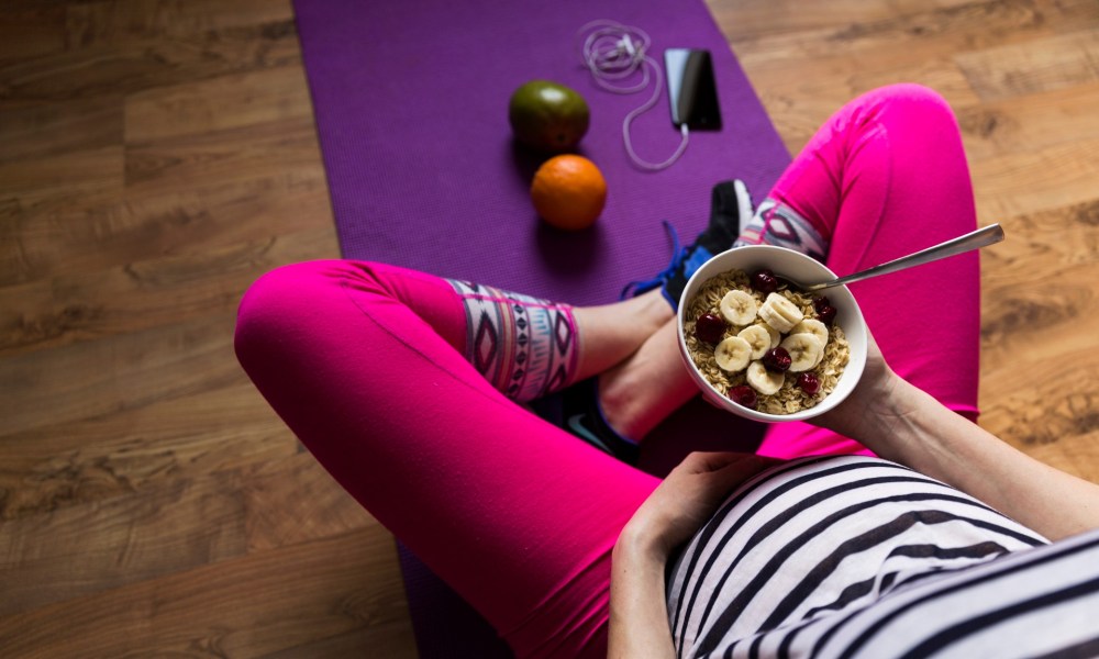 A pregnant woman sitting down eating a bowl of food.