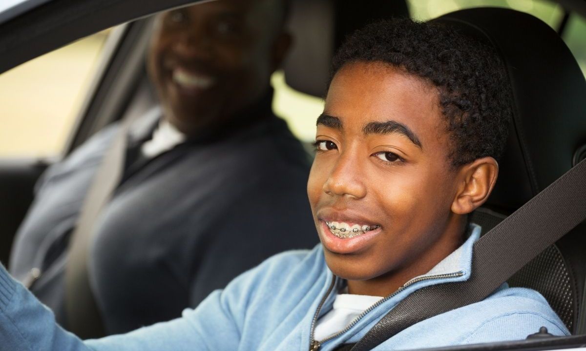 A teen boy at the wheel with Dad watching