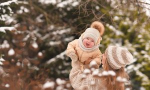 A parent holding up a baby outside in the snow