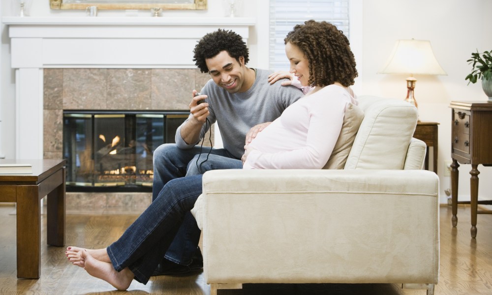 Pregnant couple sitting on the couch with a monitor.