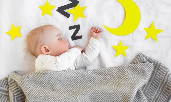 Baby sleeping in crib with a gray blanket and decals