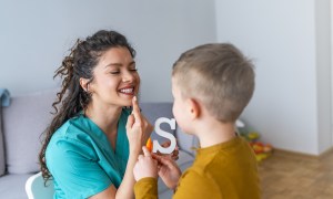 Stuttering boy and speech therapist doing exercises. Boy and young woman teacher during private home lesson. Shot of a speech therapist and a little boy