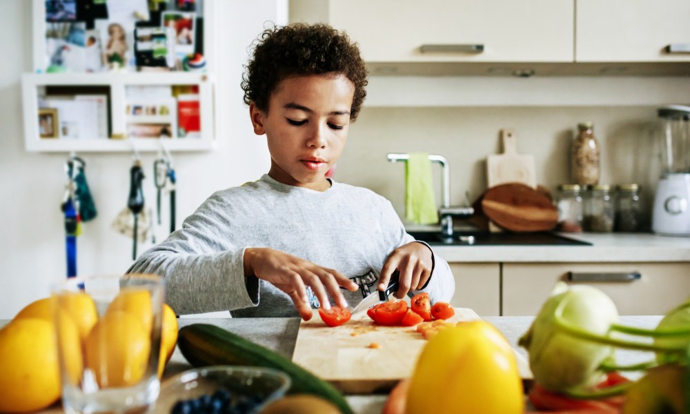 A young boy at home helping prepare lunch by slicing tomatoes