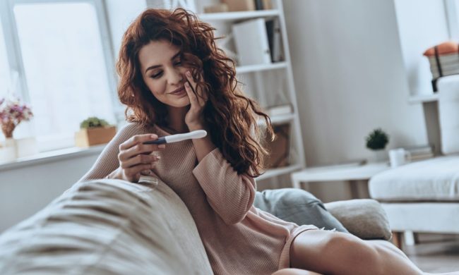 Woman sitting on couch and looking at a pregnancy test