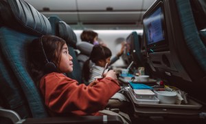 Little girl watching movie on the seat-back TV screen while enjoying her airline meal