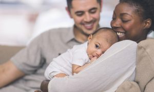 A mother holding her newborn baby with her partner looking on