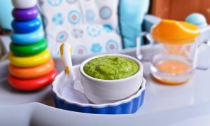 A highchair set up with a baby toy, sippy cup, and green baby food.