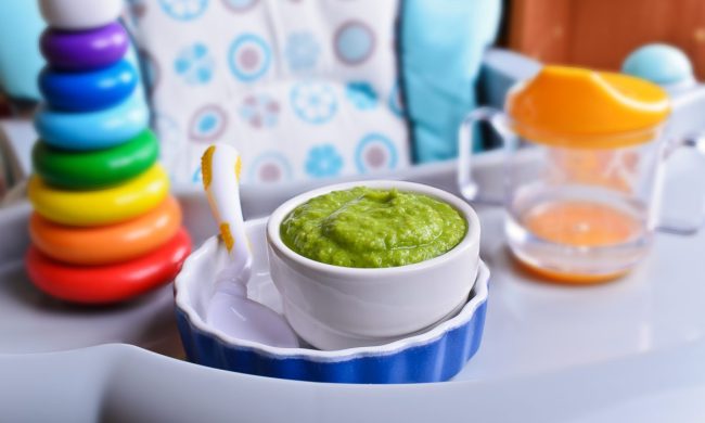 A highchair set up with a baby toy, sippy cup, and green baby food