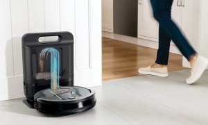 Person walking past Shark IQ self-emptying robot vacuum at docking station