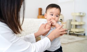 A mother taking her baby's hands out of their mouth.