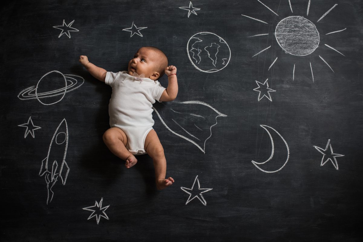 A baby laying on a chalk drawing of outer space.