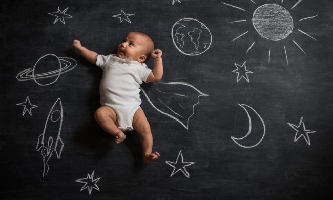 A baby laying on a chalk drawing of outer space.