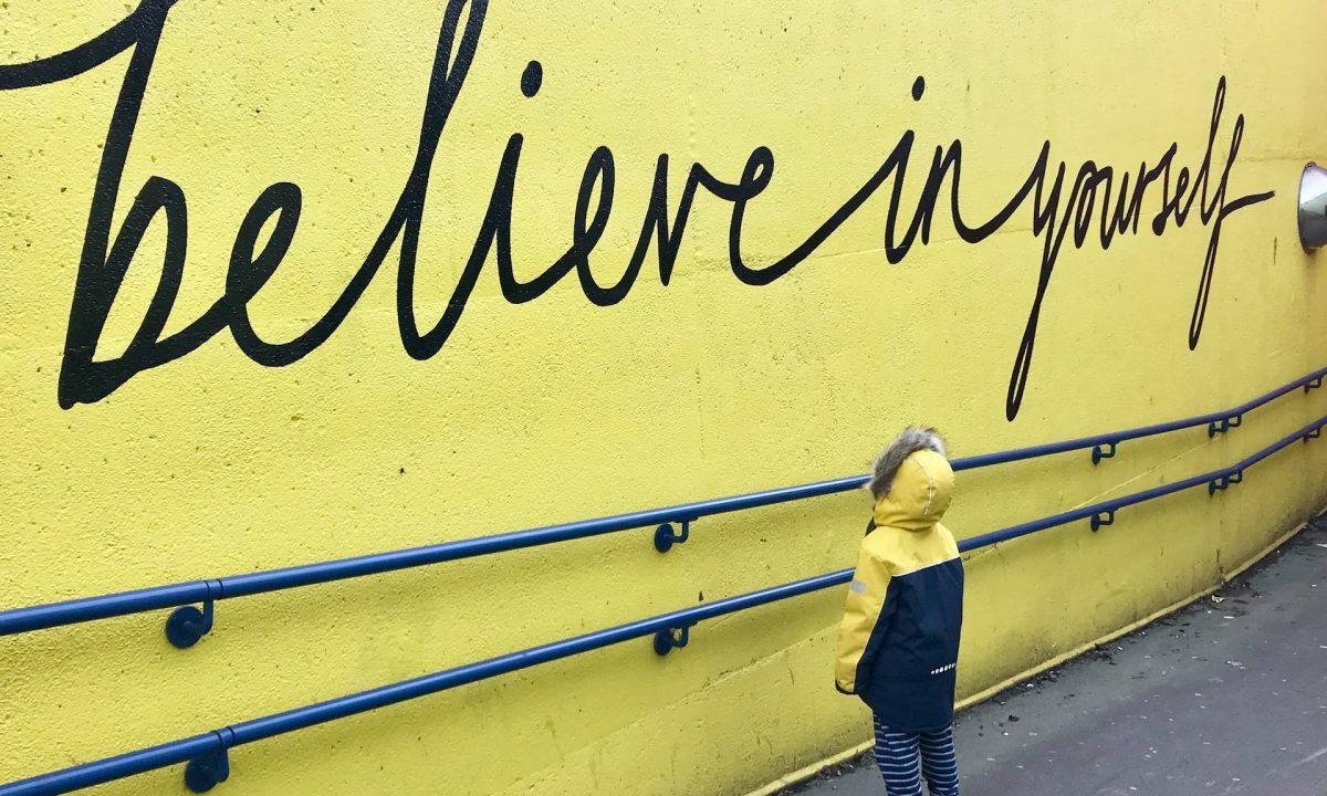 A child looking up at an affirmation written on a wall outside