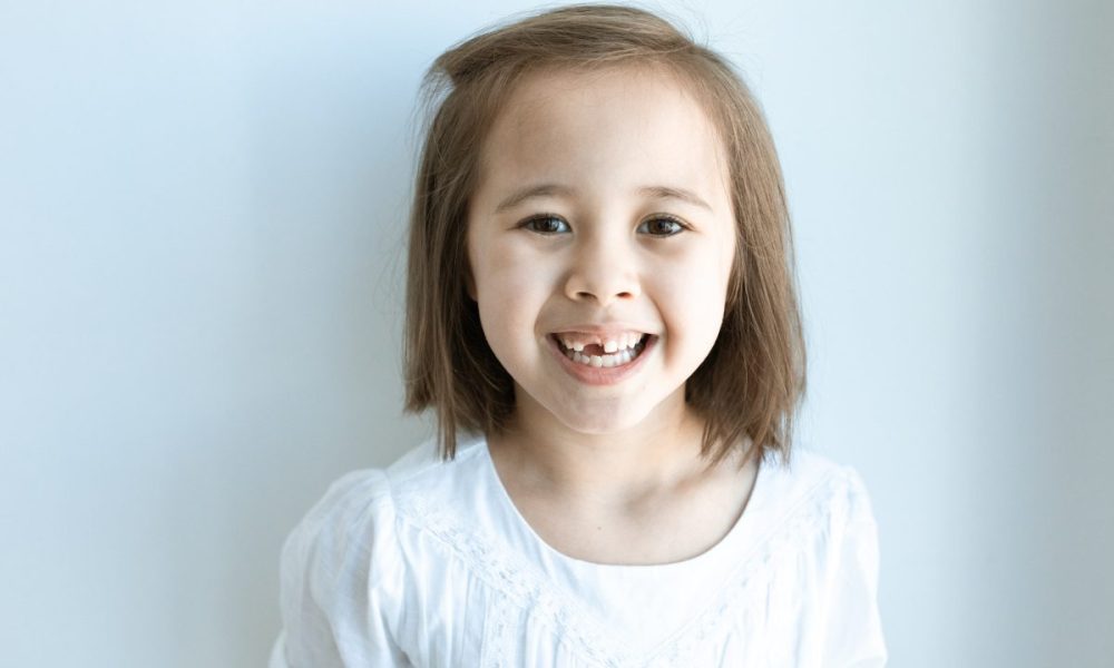 A child smiling, revealing that they are missing a tooth.