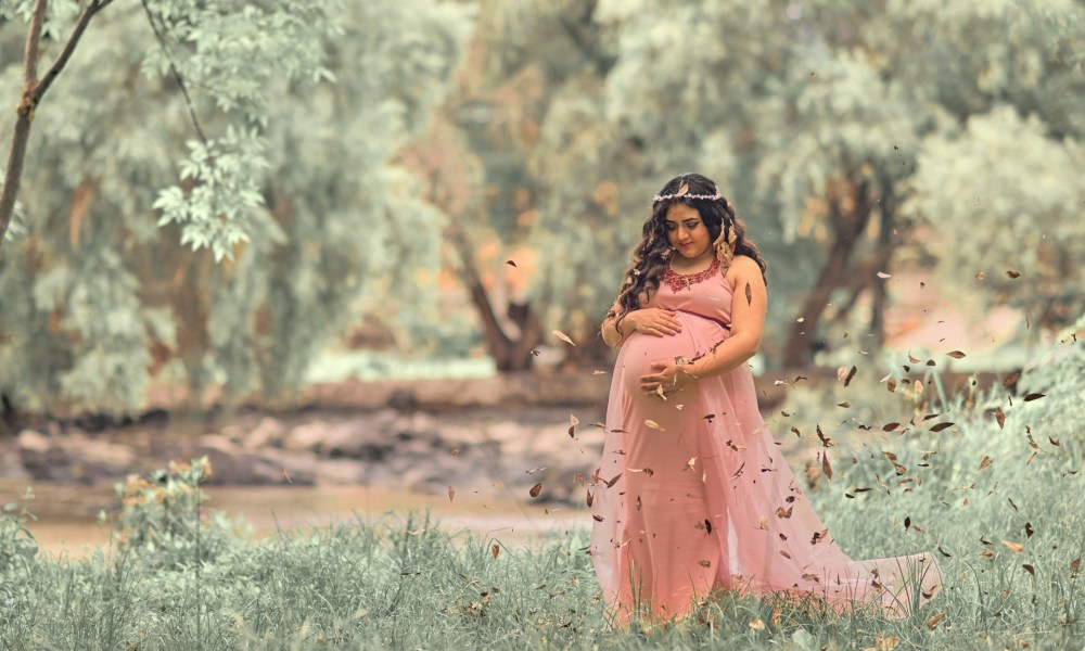 A pregnant woman outside wearing a flowing dress and headpiece.