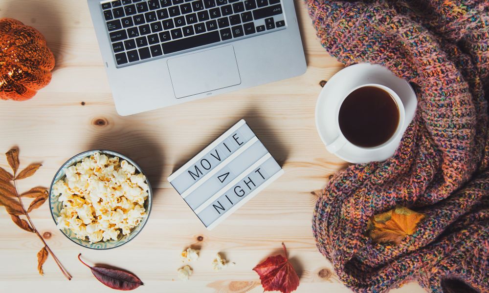 Fall movie scene with popcorn, fall leaves, scarf, and laptop