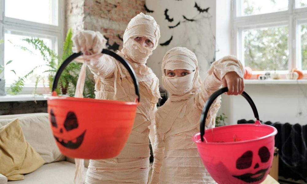 Two tweens dressed as mummies and holding pumpkin baskets