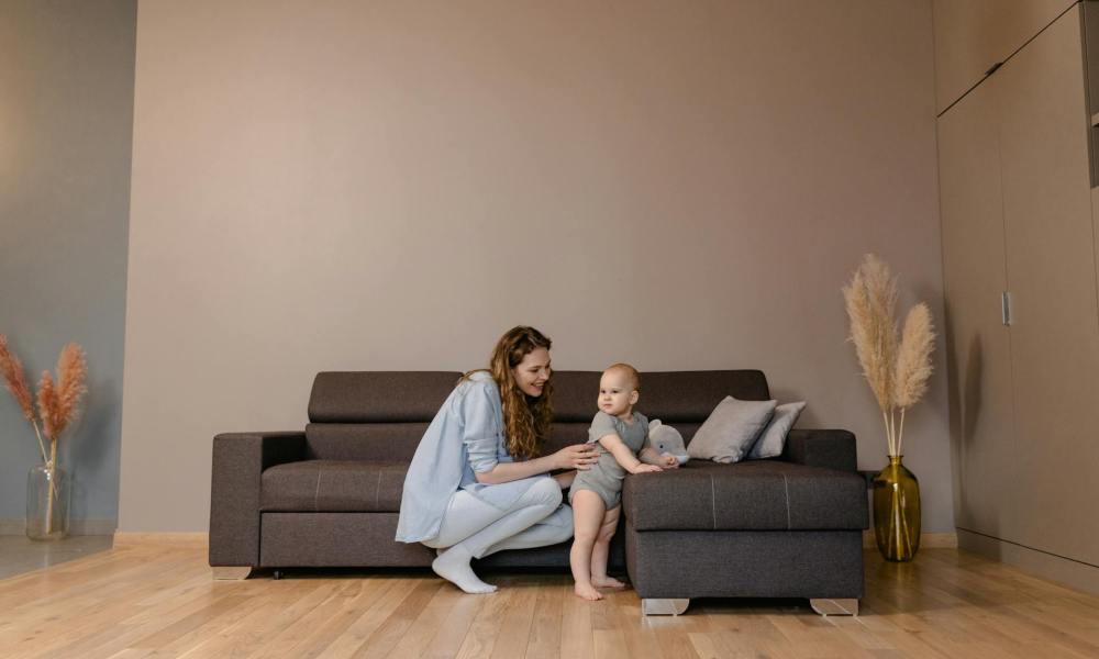 A mother helping the baby to cruise along the couch.