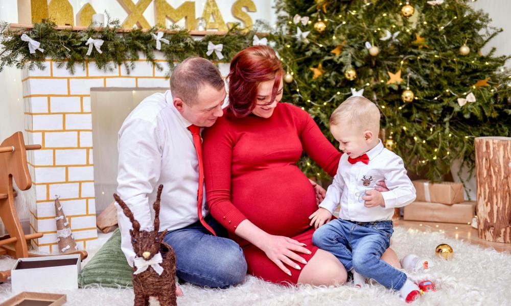 Family by the Christmas tree, mom is pregnant