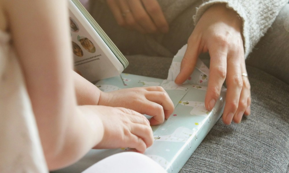 A small child opening a gift with help from a mother